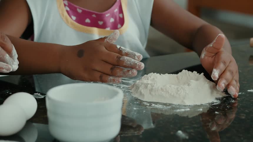 An adult and child knead flour together on a kitchen counter with flour covered hands