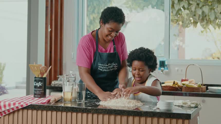 A child helps their mother knead dough in a bright kitchen