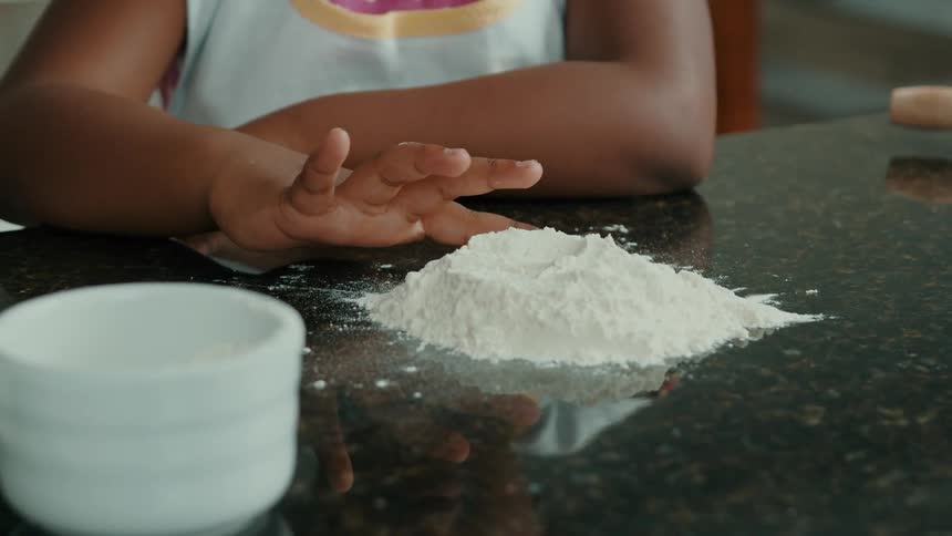Finger of a girl touching poured flour on the kitchen countertop at dawn