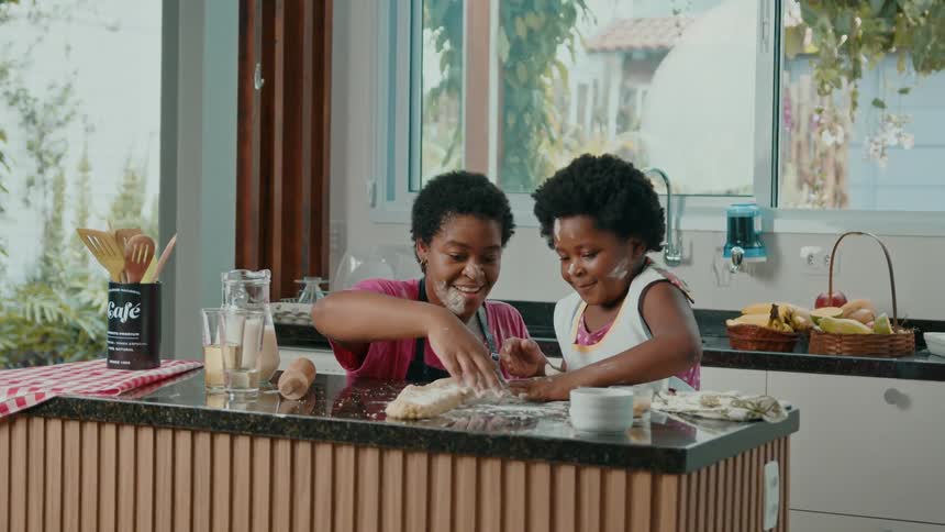 Mother playfully puts flour on her daughters face while they work on dough