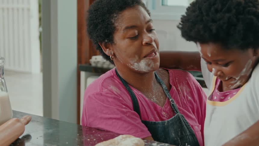 A loving mother and her young daughter their faces playfully smeared with flour share a joyful and affectionate hug while baking together in the kitchen