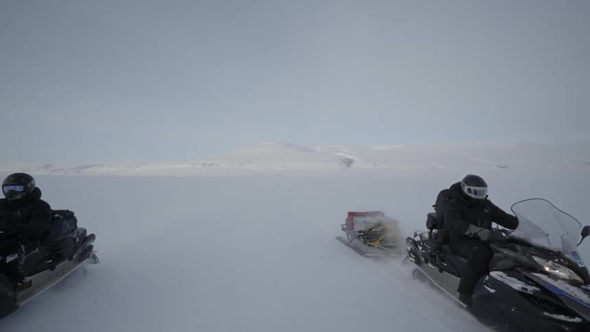 Two people ride snowmobiles in the snow