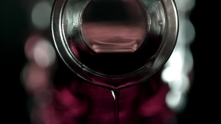 Close up of a red drink pouring from a glass bottle opening
