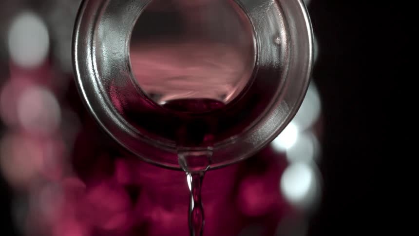 Red wine pours from the curbed spout of a glass bottle