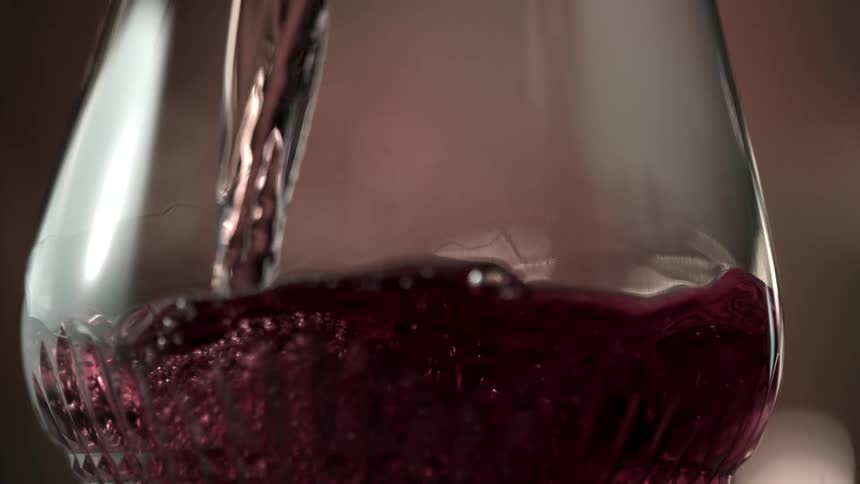 Red wine is being poured into a glass in a tight close up shot