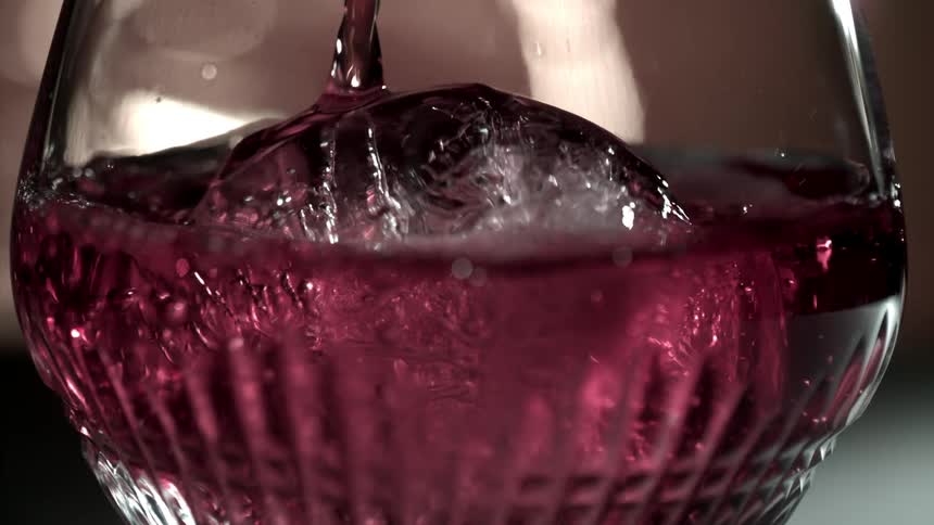 Drink being poured into a glass with an ice cube