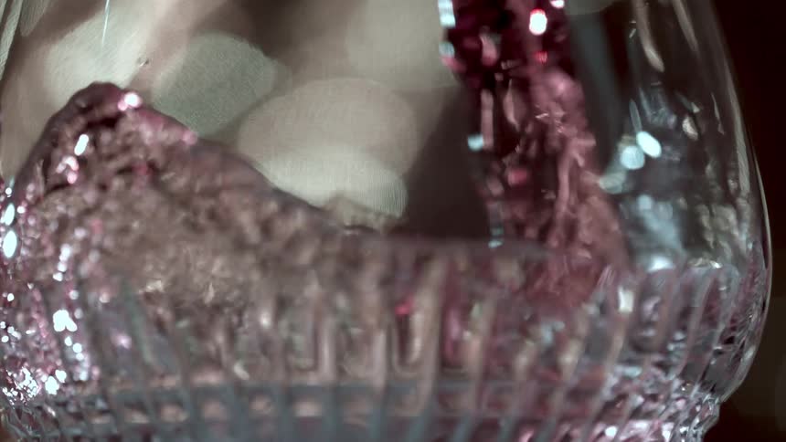 A sparkling pink liquid swirls inside a textured glass catching the light against a softfocus background