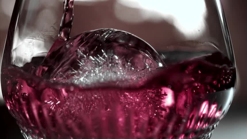 Close up of a red drink being poured into a glass cup with ice