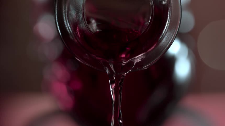 Close up of a red drink poured from a glass bottle opening