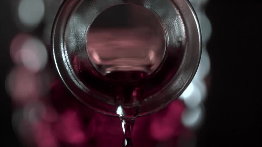Close up of a red drink being poured from a glass bottle opening