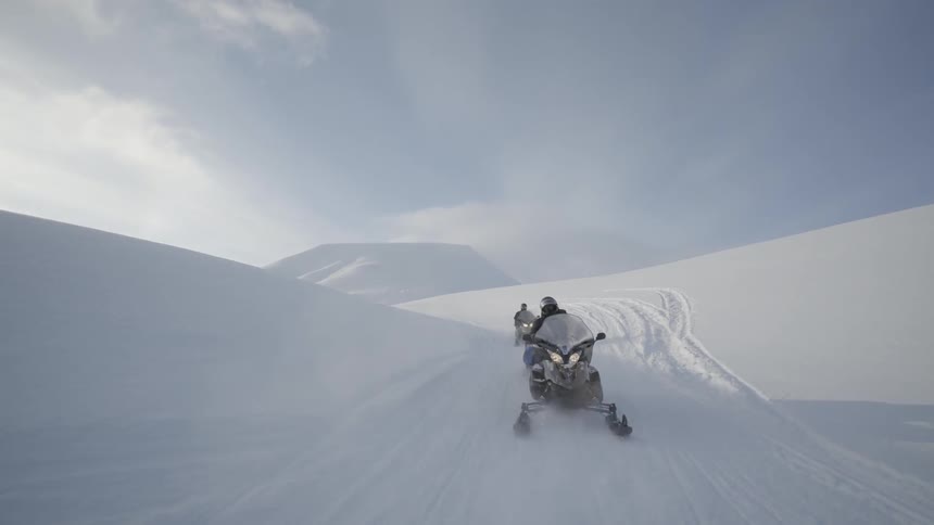 Two people ride snowmobiles in the snow