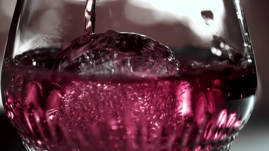 Red liquid splashes into a glass in a closeup shot