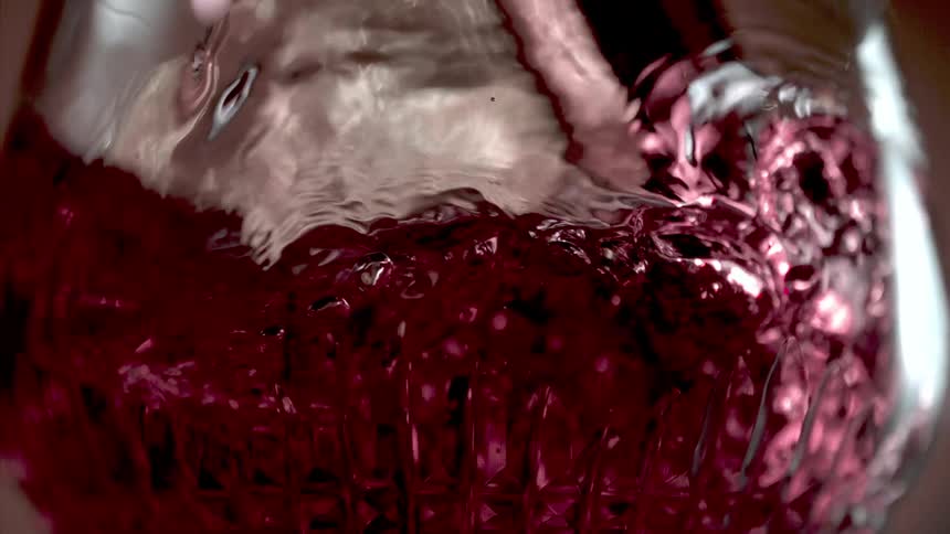 Red wine flowing into a nearly empty crystal wine glass