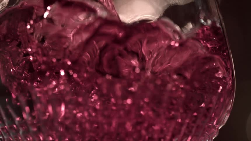 Red liquid cascades into a glass creating high splashes and vivid reflections against a dark background