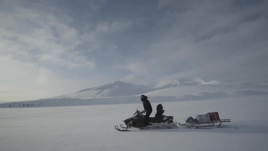 A person drives a snowmobile towing a sled in a frozen landscape