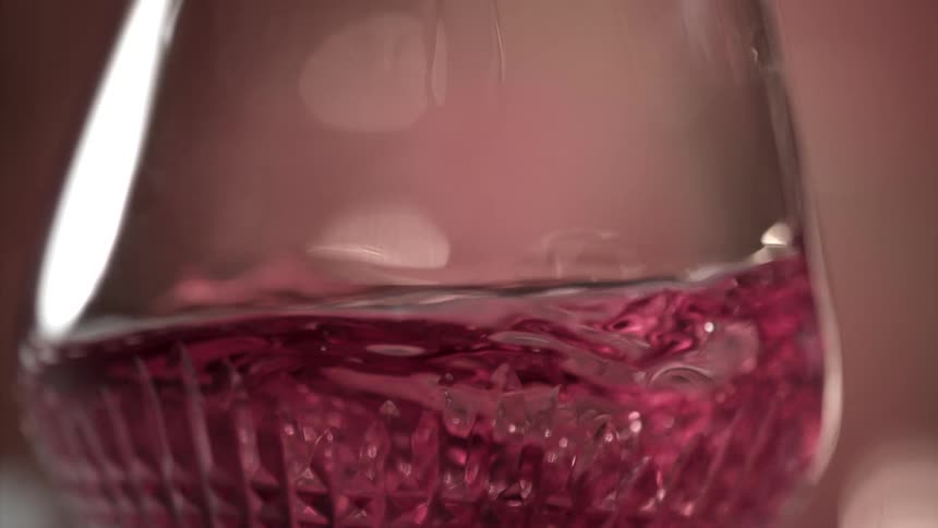 Red wine in a glass is swirled in a circular motion causing the wine to move in a circular pattern inside the glass