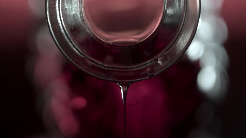Close up of a glass bottle opening raised after pouring a red drink