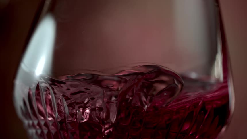 Red wine swirls in slow motion inside a crystal glass its surface moving in a gentle mesmerizing wave