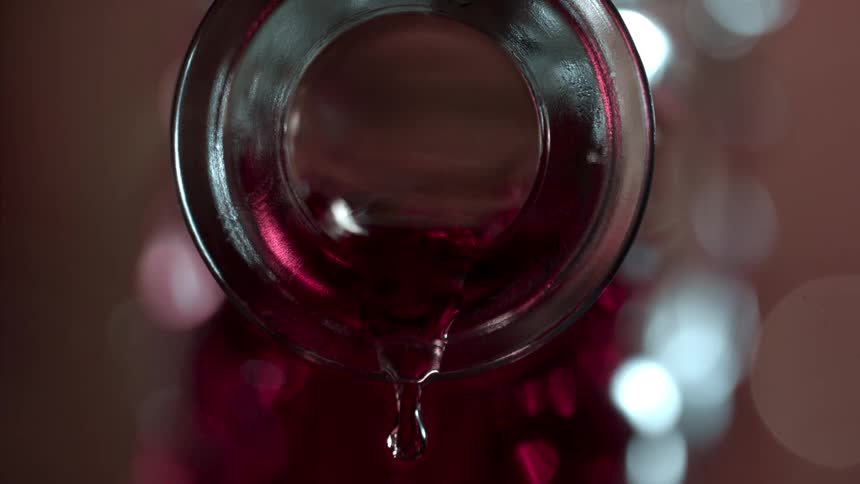 Close up of a red drink poured from a glass bottle opening
