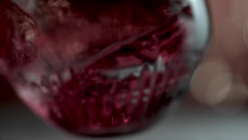 Red wine in a glass is swirled in a circular motion causing the wine to move in a circular pattern inside the glass