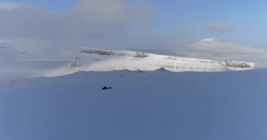 A snowmobile races on a snow covered field in the shade