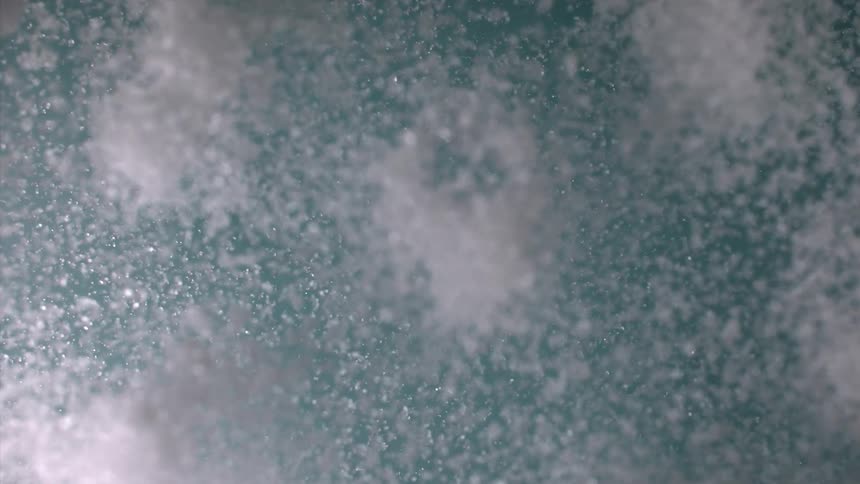 Numerous small sparkling particles are suspended in the air against a blue background