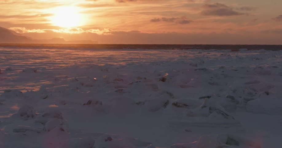 A view of a large covered field with snow and the sun setting in the back