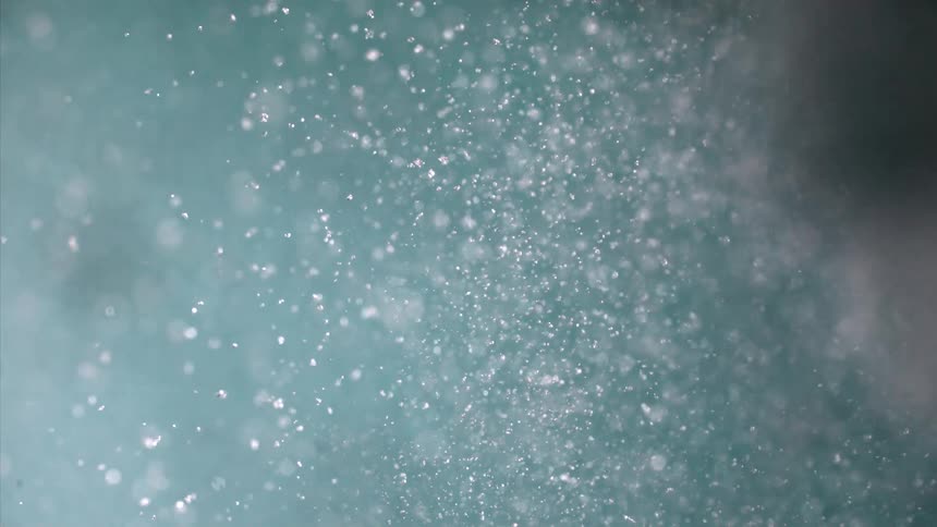 Numerous tiny sparkling particles fall through the air against a blue backdrop