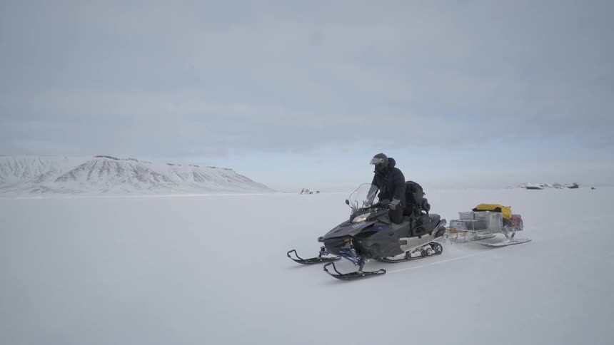A snowmobile races in the snow on a cloudy day