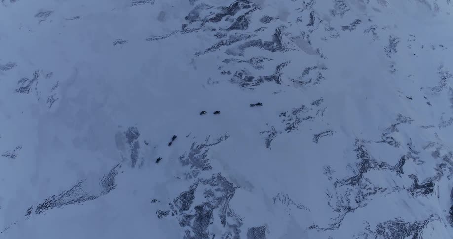 Several snowmobilers ride over a hilly, frozen landscape