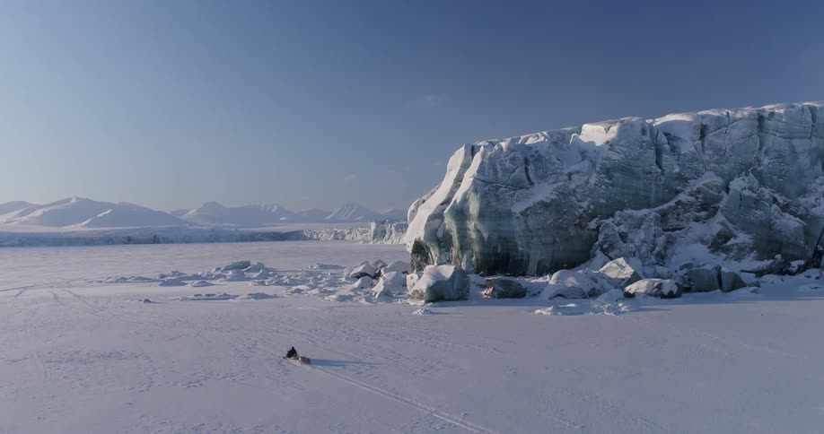 A large boulder in a field with a man snowmobiling pass it in the field
