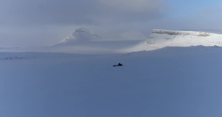 Person riding snowmobile through snow covered arctic wilderness