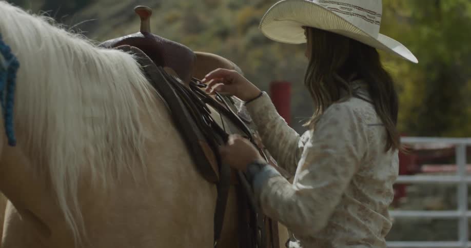 A woman is putting a saddle on her horse