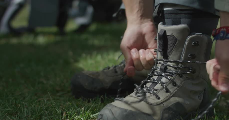 A person is tying the laces of rugged hiking boots while sitting on grass