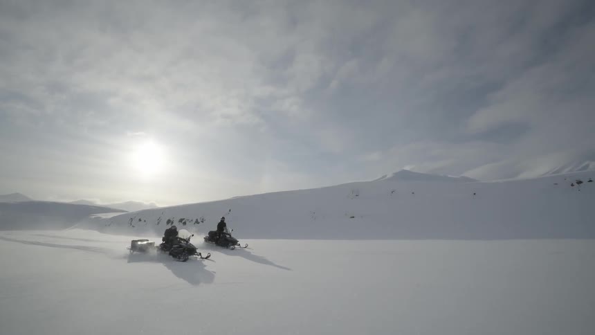 Two people ride snowmobiles in the snow