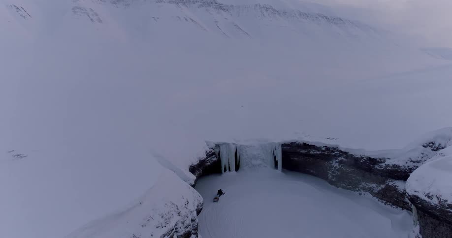 A snowmobiler rides up to a frozen waterfall