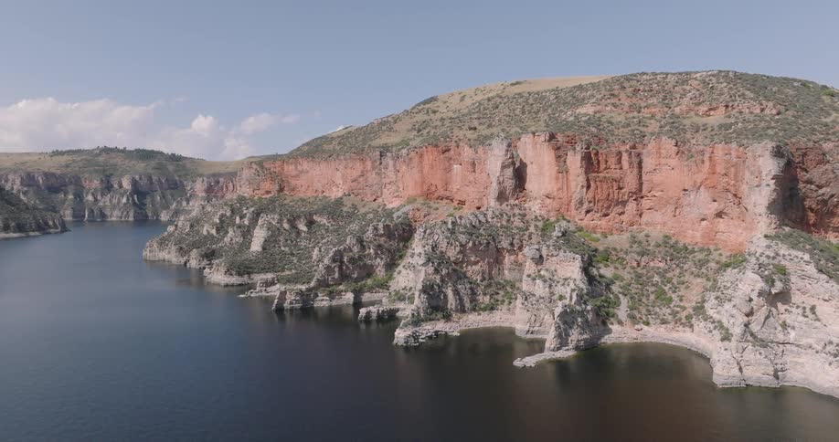 A wide view of steep rocky cliffs beside a calm body of water under a clear sky
