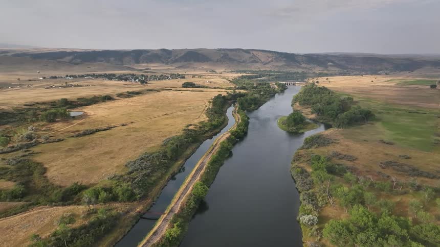 Winding river flows through golden rural fields and distant hills