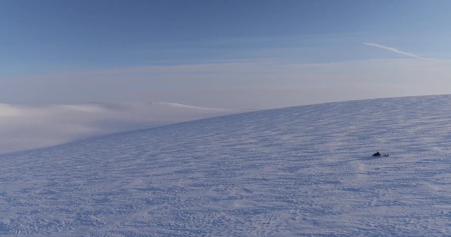 A steep hill leads to mountains as a snowmobile races down