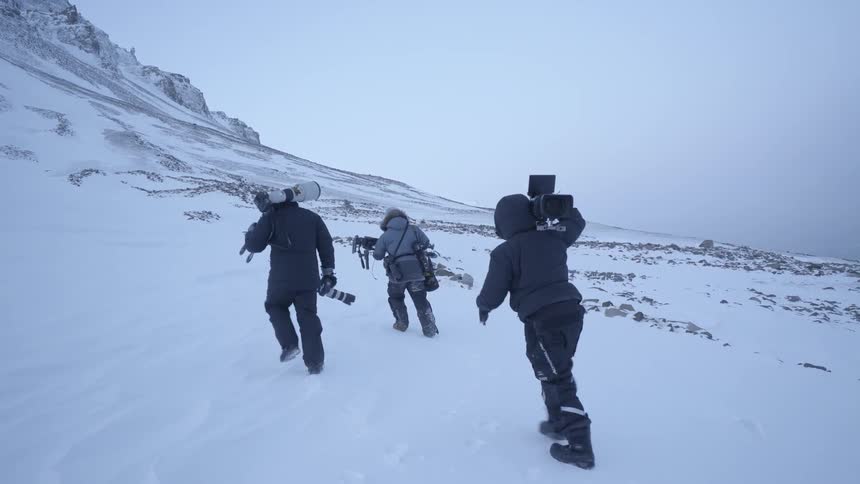 People are hiking near a snow covered mountain carrying cameras
