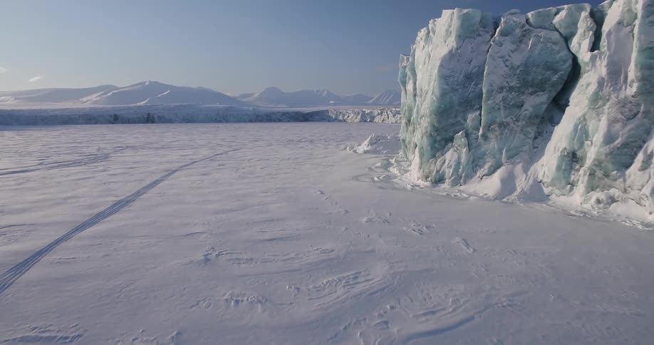 A snowmobile races along a tall ice wall