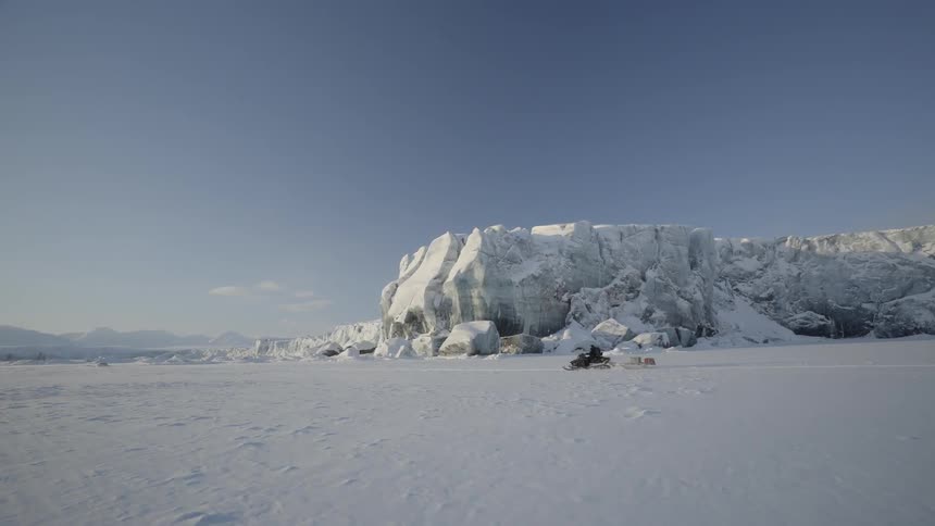 A man drives a snowmobile past an icy hill