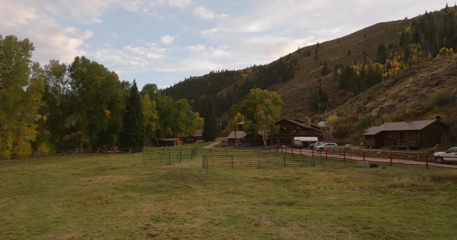 A ranch sits at the base of the mountains near the forest