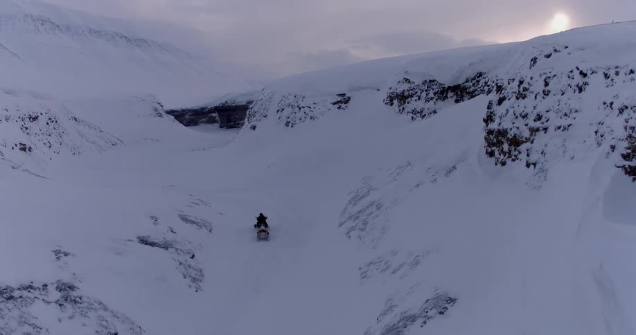 Person riding a snowmobile travels through snowy hills
