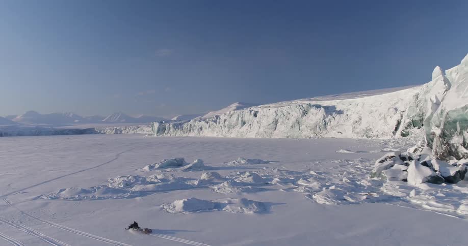Person riding snowmobile through snow covered arctic wilderness