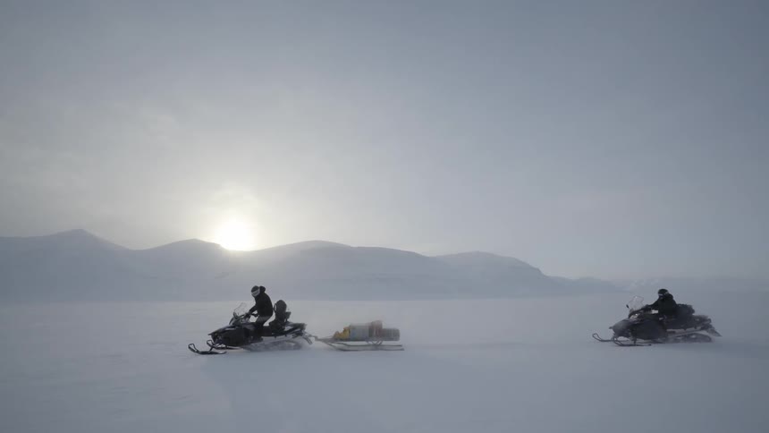 Two people riding snowmobiles in snow covered wilderness