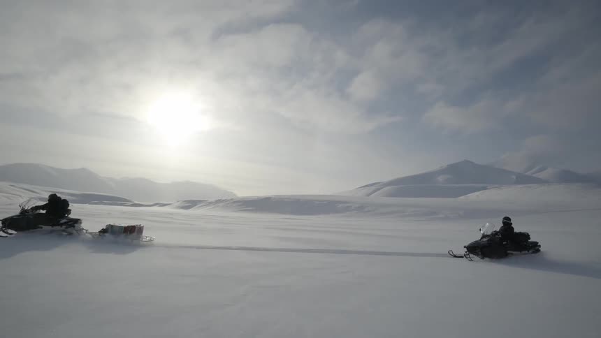 Two people ride snowmobiles in the snow