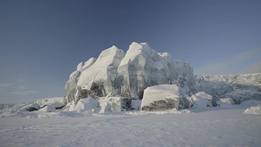 A large boulder in the middle of a snow covered field with other small boulders around it