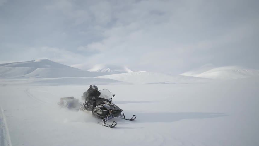 Two people ride snowmobiles in the snow