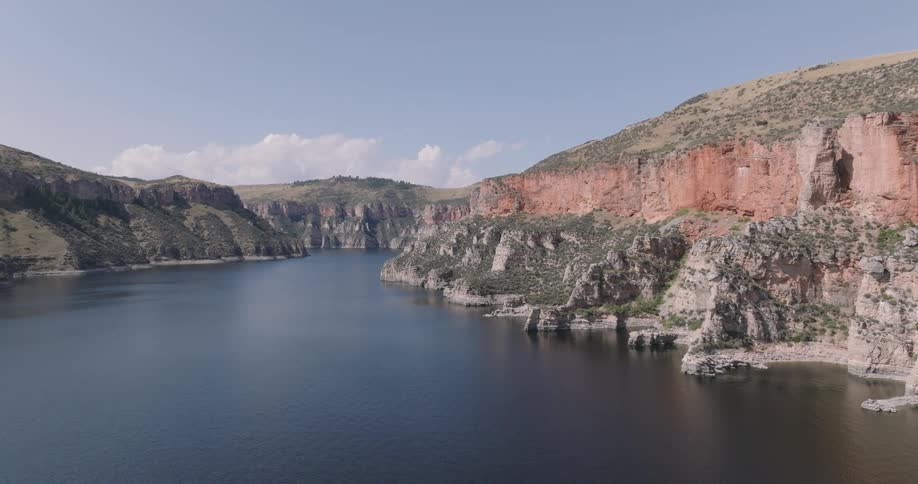 Aerial shot of a tranquil lake nestled against rugged sandstone cliffs under a clear sky